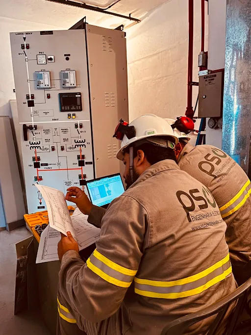 Eletricistas da PSO consultando diagrama e notebook em frente a um painel de comando de 380 V